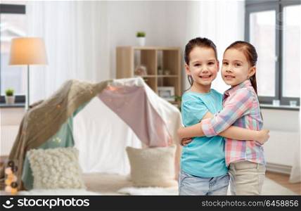 childhood, friendship and people concept - happy smiling little girls hugging at home over kids room and tepee background. happy smiling little girls hugging at home