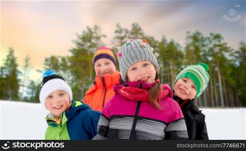 childhood, friendship and season concept - group of happy little children in winter clothes outdoors over snowy forest or park background. happy little children in winter clothes outdoors