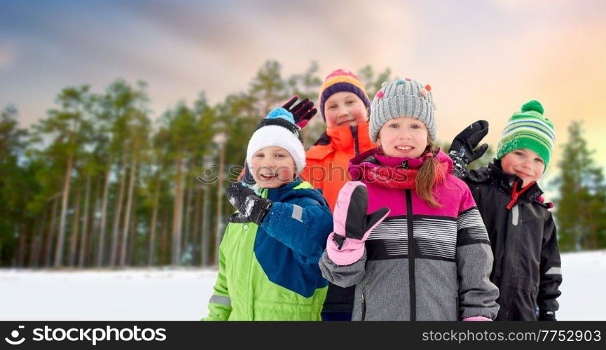 childhood, friendship and season concept - group of happy little kids in winter clothes outdoors over pine forest on background. happy little kids in winter clothes outdoors