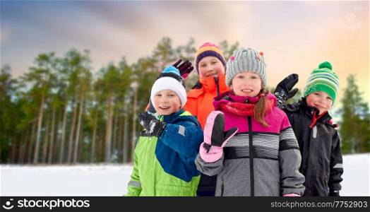 childhood, friendship and season concept - group of happy little kids in winter clothes outdoors over pine forest on background. happy little kids in winter clothes outdoors