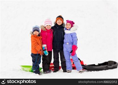 childhood, friendship and season concept - group of happy little kids with sleds hugging in winter. happy little kids with sleds hugging in winter