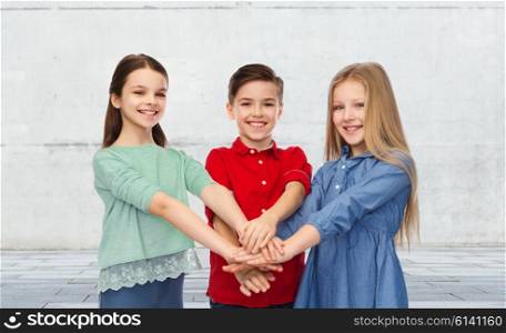 childhood, friendship, friendship and people concept - happy smiling children with hands on top over urban street background