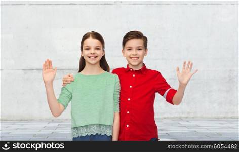 childhood, friendship, gesture and people concept - happy smiling boy and girl hugging and waving hand over urban street background