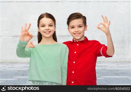 childhood, friendship, gesture and people concept - happy smiling boy and girl hugging and showing ok hand sign over urban street background