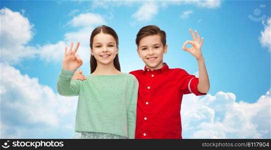 childhood, friendship, gesture and people concept - happy smiling boy and girl hugging and showing ok hand sign over blue sky and clouds background