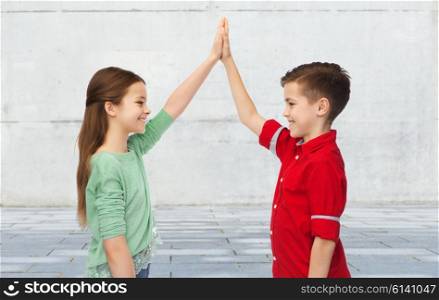 childhood, friendship, gesture and people concept - happy smiling boy and girl making high five over urban street background