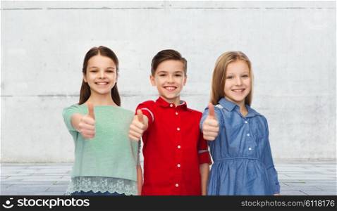 childhood, friendship, gesture and people concept - happy smiling children showing thumbs up over urban street background