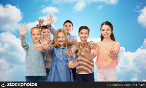 childhood, friendship, gesture and people concept - happy smiling children waving hands over blue sky and clouds background