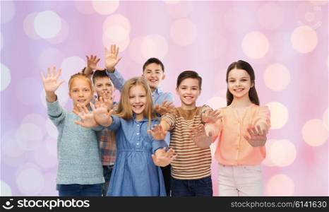childhood, friendship, gesture and people concept - happy smiling children waving hands over pink holidays lights background