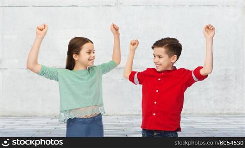 childhood, friendship, joy, gesture and people concept - happy smiling boy and girl raising fists and celebrating victory over urban street background