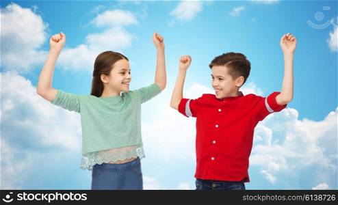 childhood, friendship, joy, gesture and people concept - happy smiling boy and girl raising fists and celebrating victory over blue sky and clouds background