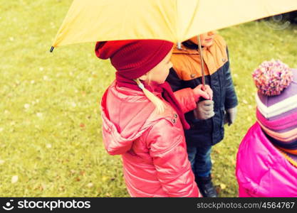 childhood, friendship, season, weather and people concept - close up of kids standing under umbrella in autumn park