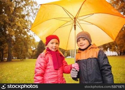 childhood, friendship, season, weather and people concept - happy little boy and girl with umbrella in autumn park
