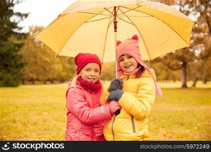 childhood, friendship, season, weather and people concept - happy little girls with umbrella in autumn park