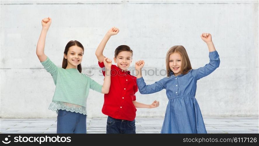 childhood, friendship, success, gesture and people concept - happy smiling boy and girls raising fists and celebrating victory over urban street background