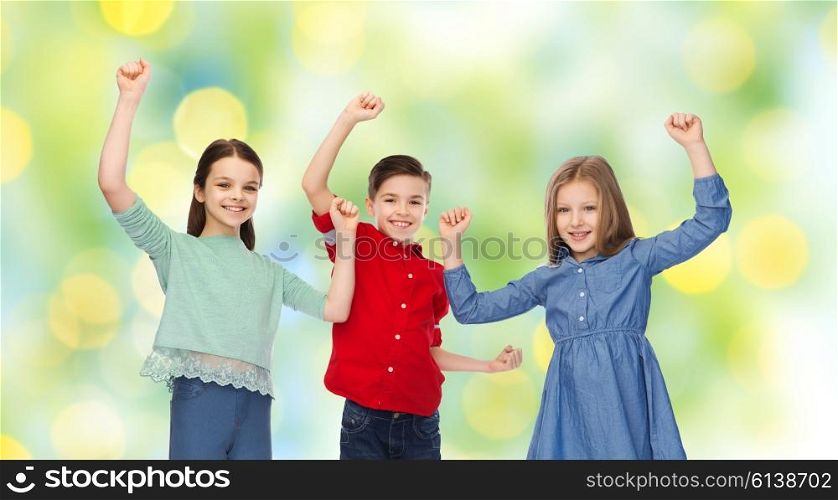 childhood, friendship, success, gesture and people concept - happy smiling boy and girls raising fists and celebrating victory over green summer holidays lights background