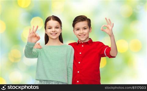 childhood, friendship, summer holidays, gesture and people concept - happy smiling boy and girl hugging and showing ok hand sign over green lights background