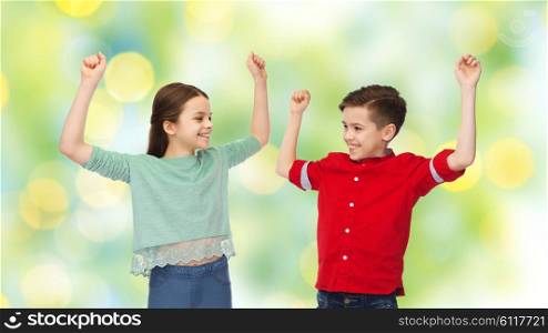 childhood, friendship, summer holidays, gesture and people concept - happy smiling boy and girl raising fists and celebrating victory over green lights background
