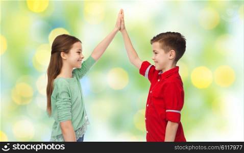 childhood, friendship, summer holidays, gesture and people concept - happy smiling boy and girl making high five over green lights background