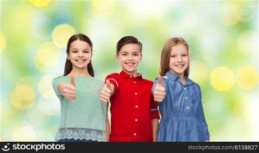 childhood, friendship, summer holidays, gesture and people concept - happy smiling children showing thumbs up over green lights background