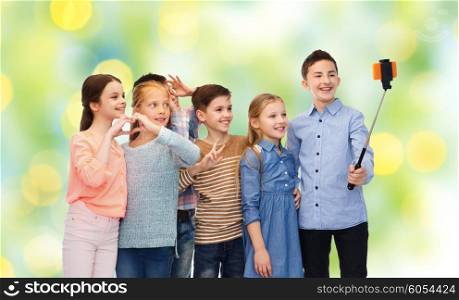 childhood, friendship, technology and people concept - happy children talking picture by smartphone on selfie stick over green lights background