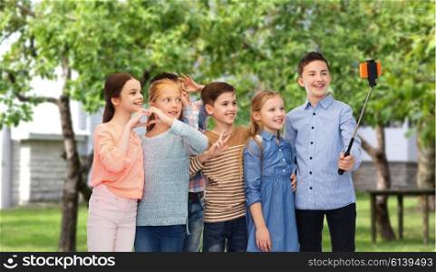 childhood, friendship, technology and people concept - happy children talking picture by smartphone on selfie stick over private house backyard background