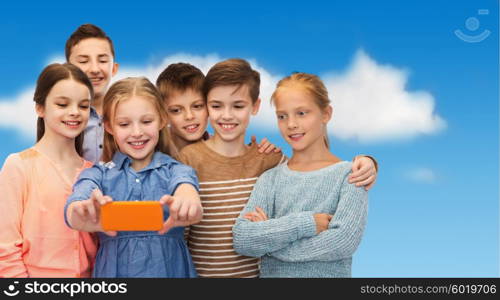 childhood, friendship, technology and people concept - happy children talking selfie by smartphone over blue sky and clouds background
