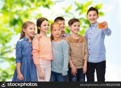 childhood, friendship, technology and people concept - happy children talking selfie by smartphone over green natural background