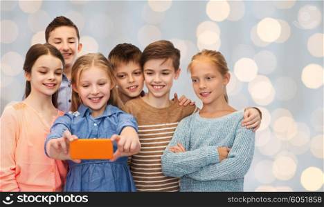 childhood, friendship, technology and people concept - happy children talking selfie by smartphone over holidays lights background