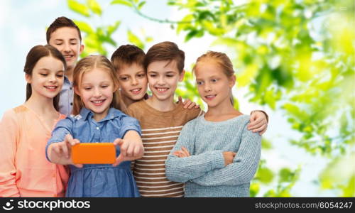 childhood, friendship, technology and people concept - happy children talking selfie by smartphone over green natural background