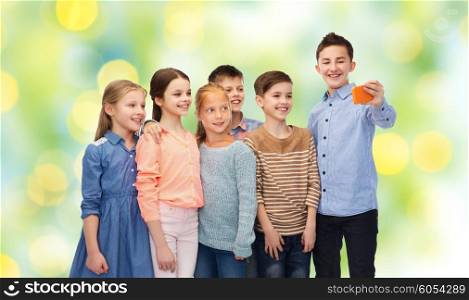 childhood, friendship, technology and people concept - happy children talking selfie by smartphone over green lights background