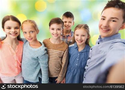 childhood, friendship, technology and people concept - happy children talking selfie over green lights background