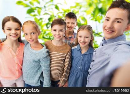 childhood, friendship, technology and people concept - happy children talking selfie over green natural background