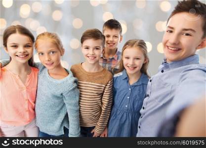 childhood, friendship, technology and people concept - happy children talking selfie over holidays lights background