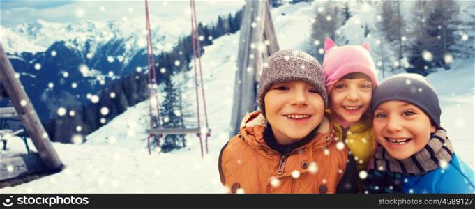 childhood, friendship, winter holidays, vacation and people concept - group of happy kids hugging over swing and snowy mountains background