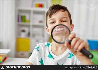 childhood, fun and curiosity concept - happy little boy with magnifier showing big teeth at home. boy with magnifier showing big teeth at home
