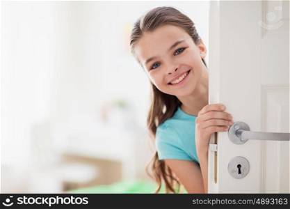 childhood, fun and people concept - happy smiling beautiful girl behind door at home