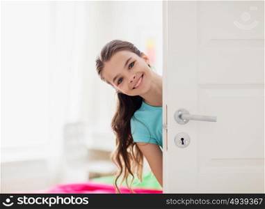 childhood, fun and people concept - happy smiling beautiful girl behind door at home. happy smiling beautiful girl behind door at home