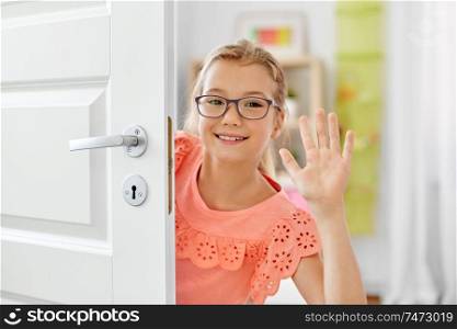 childhood, fun and people concept - happy smiling beautiful girl in glasses behind door waving hand at home. happy smiling beautiful girl behind door at home