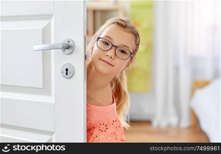 childhood, fun and people concept - happy smiling beautiful girl in glasses behind door at home. beautiful girl l in glasses behind door at home