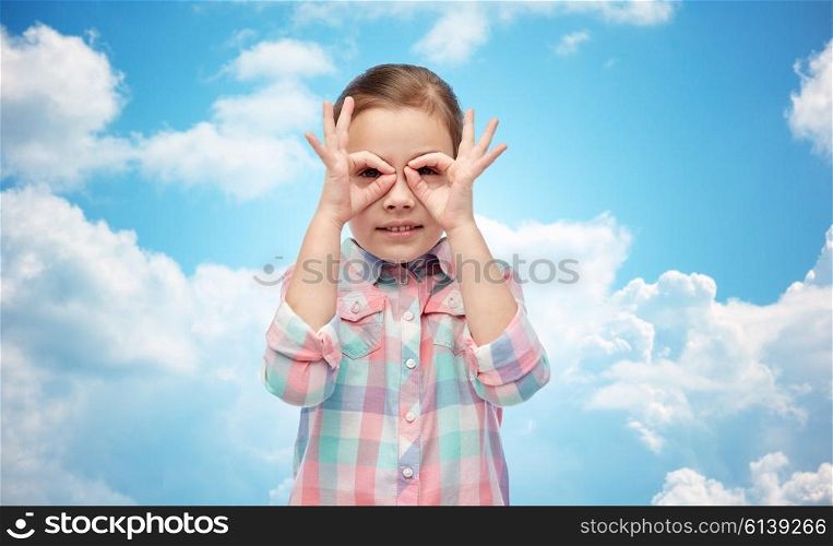 childhood, fun, gesture and people concept - happy little girl making faces over blue sky and clouds background