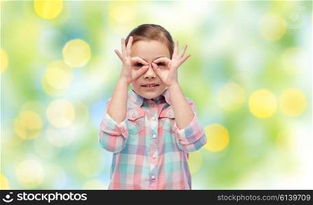 childhood, fun, gesture and people concept - happy little girl making faces over summer green lights background