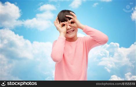 childhood, fun, gesture and people concept - happy little girl making faces over blue sky and clouds background