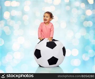 childhood, game, sport, football and people concept - happy african american little baby girl playing with ball over blue holidays lights background