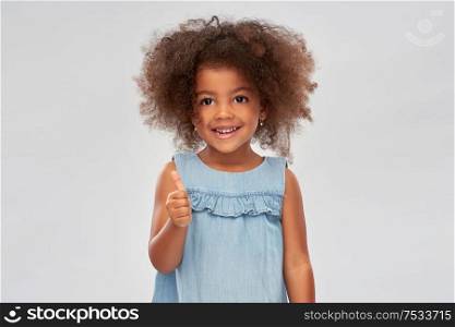 childhood, gesture and people concept - happy little african american girl showing thumbs up over grey background. little african american girl showing thumbs up