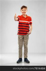 childhood, gesture and people concept - portrait of happy smiling boy in red polo t-shirt showing thumbs up over grey background. happy boy in red polo t-shirt showing thumbs up