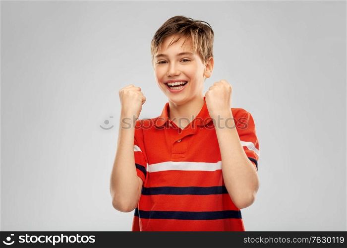childhood, gesture and people concept - portrait of happy smiling boy in red polo t-shirt celebrating success over grey background. portrait of happy smiling boy celebrating success