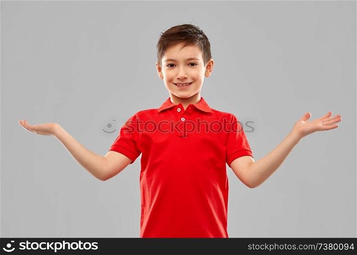 childhood, gesture and people concept - portrait of smiling little boy in red polo t-shirt holding something imaginary on empty hands over grey background. smiling boy holding something on empty hands