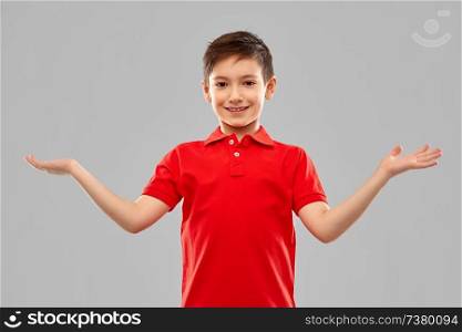 childhood, gesture and people concept - portrait of smiling little boy in red polo t-shirt holding something imaginary on empty hands over grey background. smiling boy holding something on empty hands