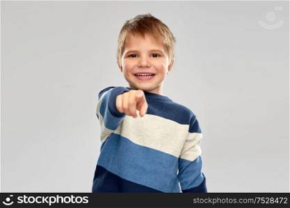 childhood, gesture and people concept - portrait of smiling little boy in striped pullover pointing finger over grey background. little boy in striped pullover pointing finger